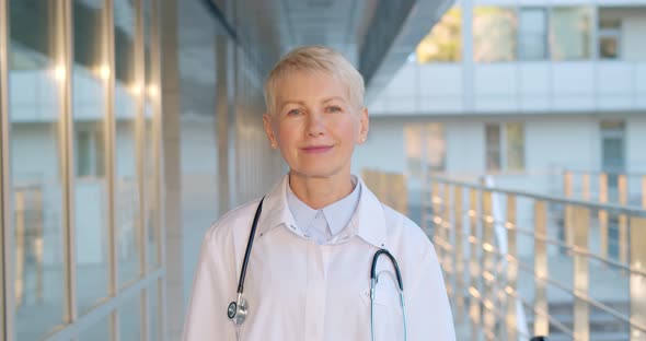 Portrait of Happy Caucasian Female Doctor Standing Outside Hospital Building and Smiling at Camera