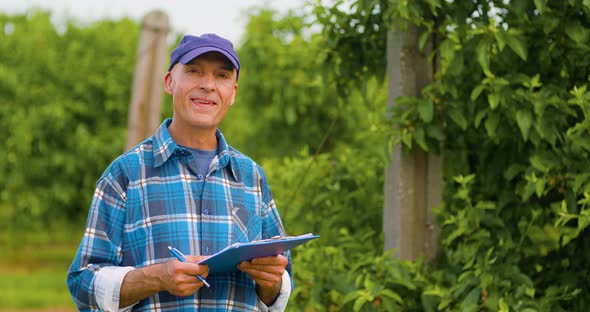 Male Researcher Looking at Trees While Writing on Clipboard