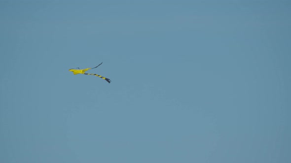 A bright yellow kite flying in clear sky