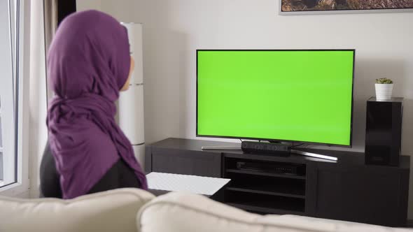 A Muslim Woman Celebrates As She Watches TV with Green Screen in an Apartment  View From Behind