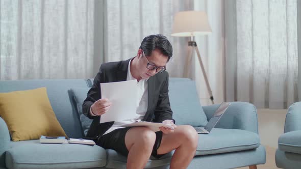 Asian Businessman In Jacket And Shorts Checking The Documents While Working A Laptop At Home