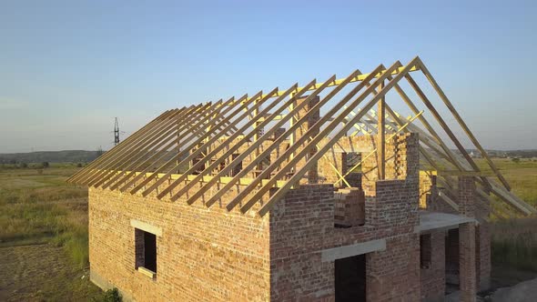 Aerial view of unfinished brick house with wooden roof structure under construction.