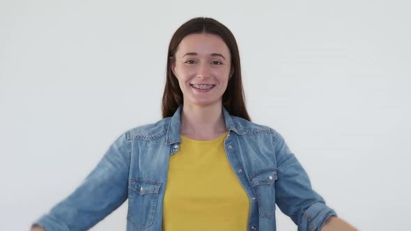 Happy Woman Folds Her Hands in Heart in Front of Her Smile in Braces on White Background