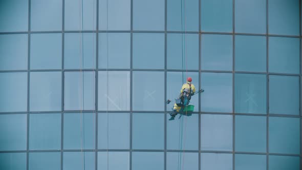 A Man Worker Hanging on Ropes By the Exterior Windows of a Skyscraper and Cleaning Them - Industrial