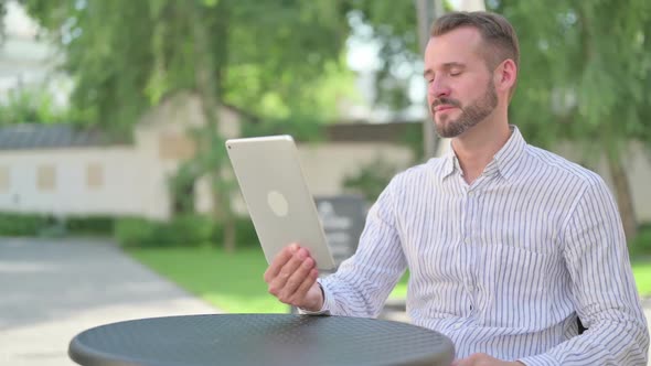 Middle Aged Man Making Video Call on Tablet in Outdoor Cafe