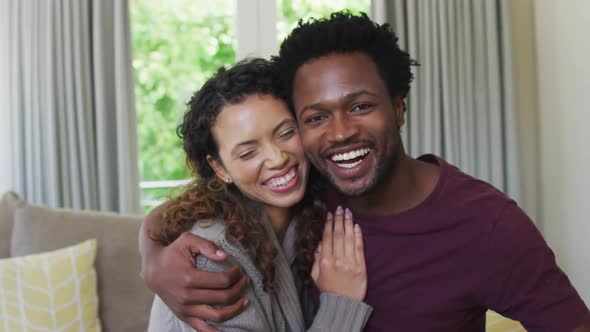 Portrait of happy biracial couple looking at camera, embracing and smiling