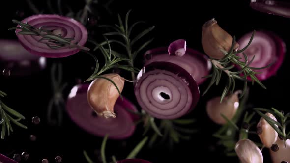 Slow Motion Flying Onion Rings and Garlic Cloves with Rosemary and Spices on a Black Background