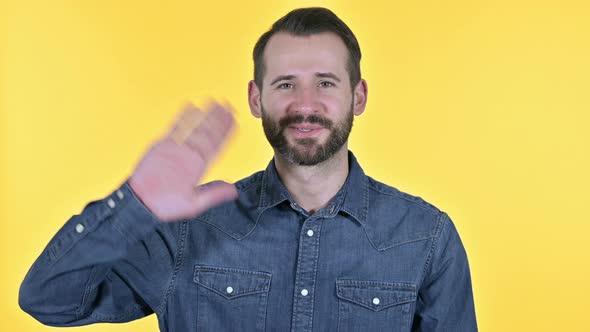 Beard Young Man Waving at the Camera, Yellow Background
