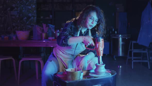 Woman with Curly Hair Heating Up a Fresh New Pot on the Potter's Wheel