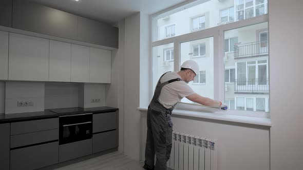 A Builder in Uniform Checks the Size and Quality of Window Installation in a New Apartment