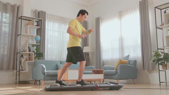 Side View Of Asian Man Training On Walking Treadmill And Looking Smart Watch At Home