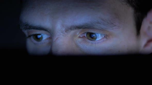 Male in Hat Looks at a Laptop Monitor at Night