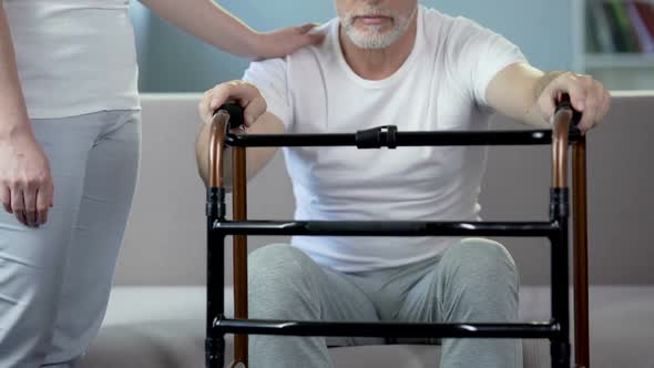 Nurse supporting old man holding walking frame, rehabilitation center. Pensioner