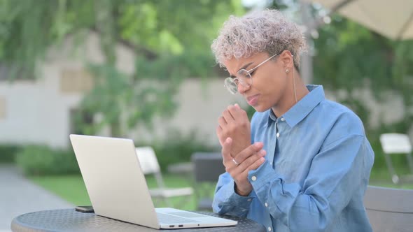 Young African Woman with Laptop Having Wrist Pain in Outdoor Cafe