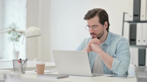 Young Man with Laptop Thinking at Work