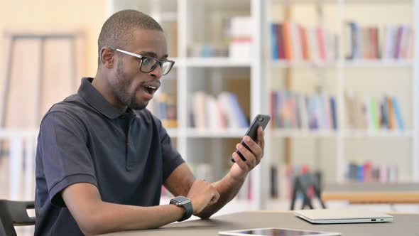 Ambitious Young African Man Celebrating Success on Smart Phone