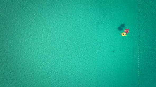 Aerial view of man and woman floating by string buoy on inflatable mattresses.