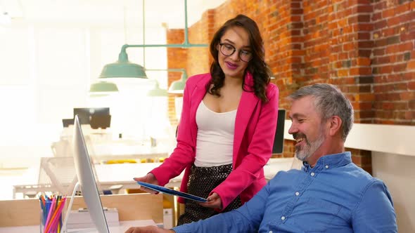 Male and female executives discussing over digital tablet at desk