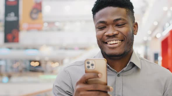 Happy Smiling Guy Walks Indoors Reads Good Email Message on Phone Uses Free Wifi Chatting in Social