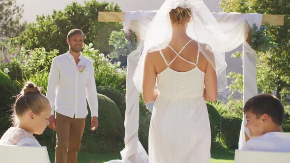 Caucasian bride walking to outdoor altar to groom and wedding officiant