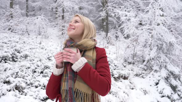 Beautiful blonde woman with cup of coffee in snow forest