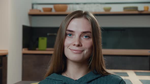 Close-up Portrait of Happy Young Woman with Blue Eyes Sitting in Living Room Smiling and Looking 