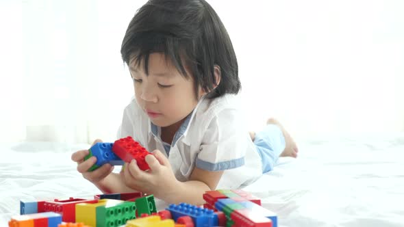 Little Asian Child Playing With Colorful Construction Blocks On White Bed