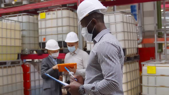 African Manager in Safety Helmet with Clipboard Doing Inventory in Large Warehouse