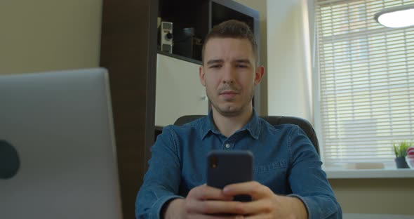 Man Sitting at His Desk Home on Desktop Computer. Starts Using Smartphone, Uses Social Media App