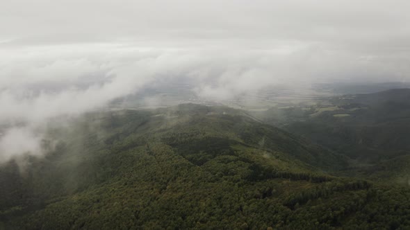 Backward flying over green forest through clouds, Wide aerial shot, Slovakia