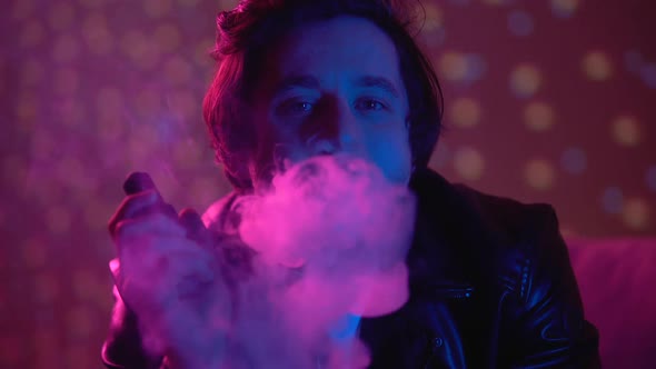 Thoughtful Unhappy Man Vaping E-Cigarette, Exhaling Smoke in Nightclub Lights