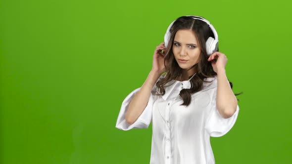 Girl Listens Through the Headphones Music and Whirl Around Her. Green Screen