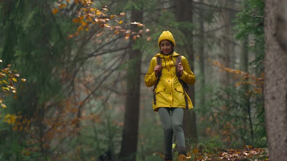 Pretty Woman in Yellow Jacket and Beany with Tourist Backpack Walking Through Wet Autumn Forest Wild