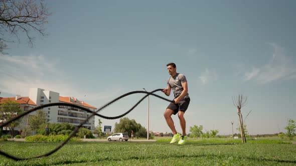 Muscular Caucasian Athlete Makes Waves with a Battle Rope on the Grass Outside