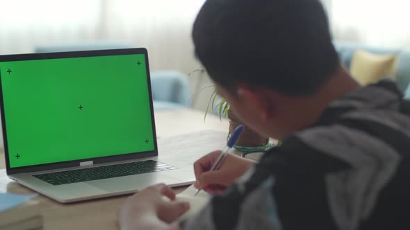 Boy Sitting At His Desk Learning Online On A Laptop With Green Mock-Up Screen