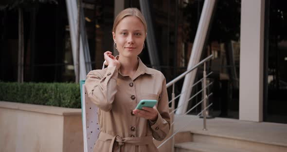Portrait of Blonde Hair Woman Raising Head and Looking To Camera While Using Her Smartphone