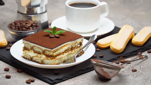 Portion of Traditional Italian Tiramisu dessert and mocha coffee maker on grey concrete background