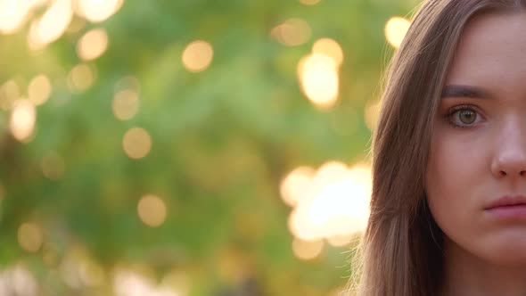 Close up of the half female face with long brown hair looking in the camera and then smiling outdoor