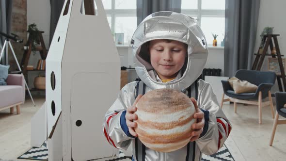 Kid in Spacesuit Holding Model of Planet and Smiling