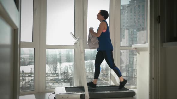 Woman is intense training on treadmill at home. Young female wipes sweat with towel