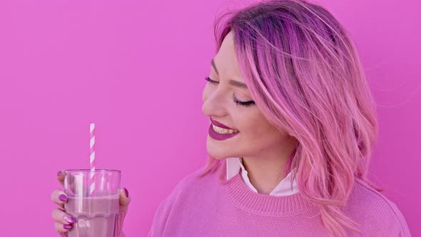 Pink woman holding milkshake in front of pink wall