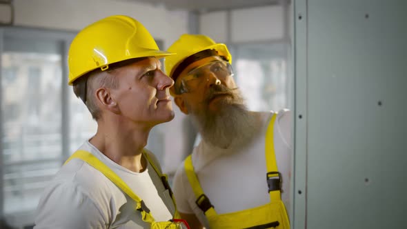 Builder and Foreman in Safety Uniform Examining Drywall at Construction Site