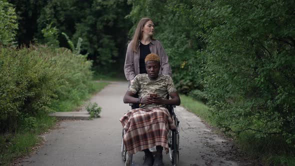 Beautiful Caucasian Woman Pushing Wheelchair with African American Man Talking in Slow Motion