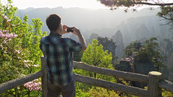 Man Tourist Taking Pictures of Mountain Landscape at Sunset with His Smartphone