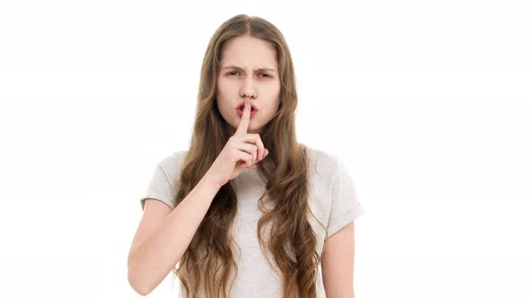 Portrait of Serious Brunette Schoolgirl with Long Hair Holding Index Finger on Lips and Asking to