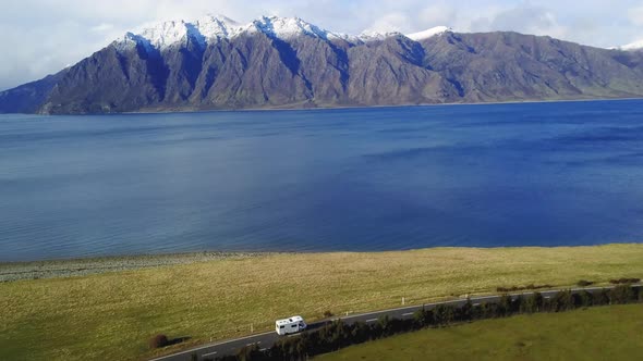 Aerial video of a Van driving on a Coastal road with green paddocks, then panning to the blue ocean,