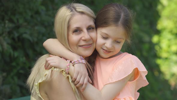 Portrait of Blond Mother and Her Little Daughter Hugging in the Summer Park Looking at Camera