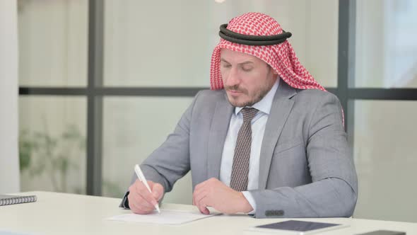 Middle Aged Arab Businessman Thinking while Writing on Paper in Office