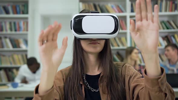 Female Student in Augmented Reality Goggles Sitting in the Library and Moving Hands