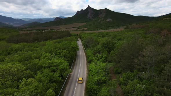 A Car Drives Down a Paved Road in a Mountainous Area That Cuts Through a Forest